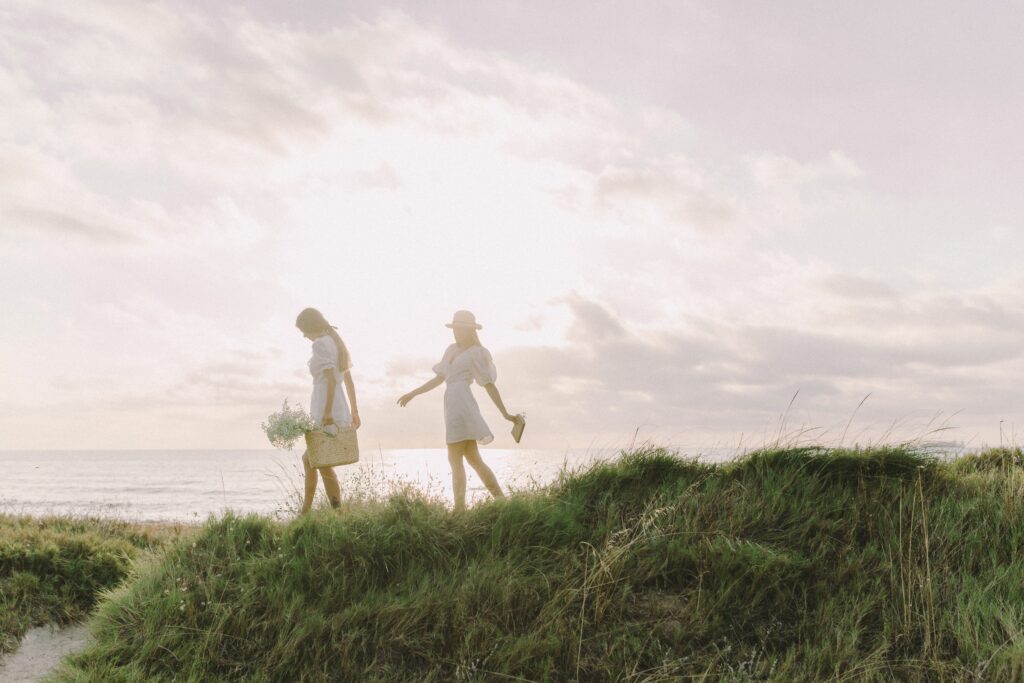 2 Women Walking along grass field in front of beach